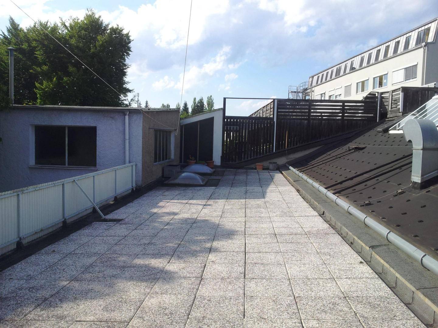 Geräumige Dachterrasse mit Fliesenboden, umgeben von Gebäuden und Bäumen.
