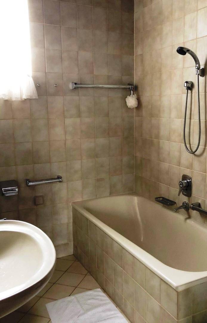 Badezimmer mit beigefarbenen Fliesen, Badewanne mit Duschfunktion und Fenster.