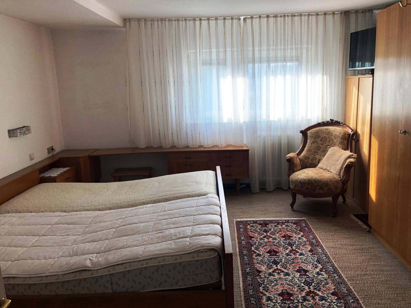 Schlafzimmer mit zwei Betten, großem Kleiderschrank und einem Fenster mit Vorhängen.
