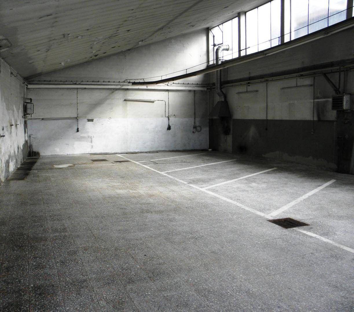 Weitläufige Halle mit Parkplatzmarkierungen, hohen Fenstern und viel Tageslicht.