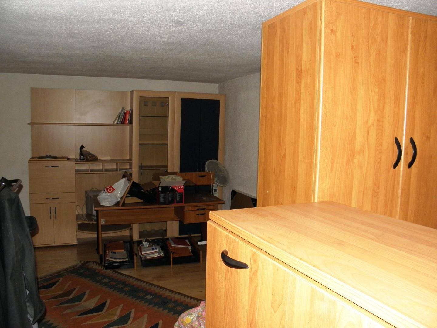 Zimmer mit hellen Holzmöbeln, Schreibtisch und einem farbenfrohen Teppich.