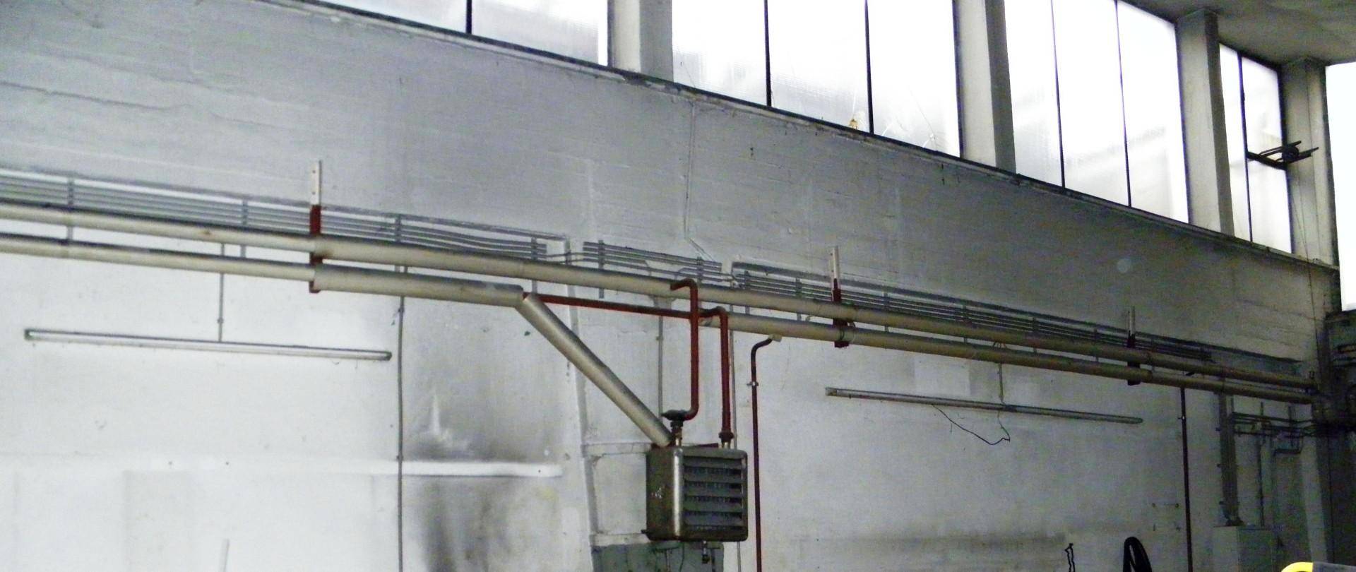 Industrieller Raum mit langen Rohrleitungen, hohen Fenstern und einem Heizgerät.