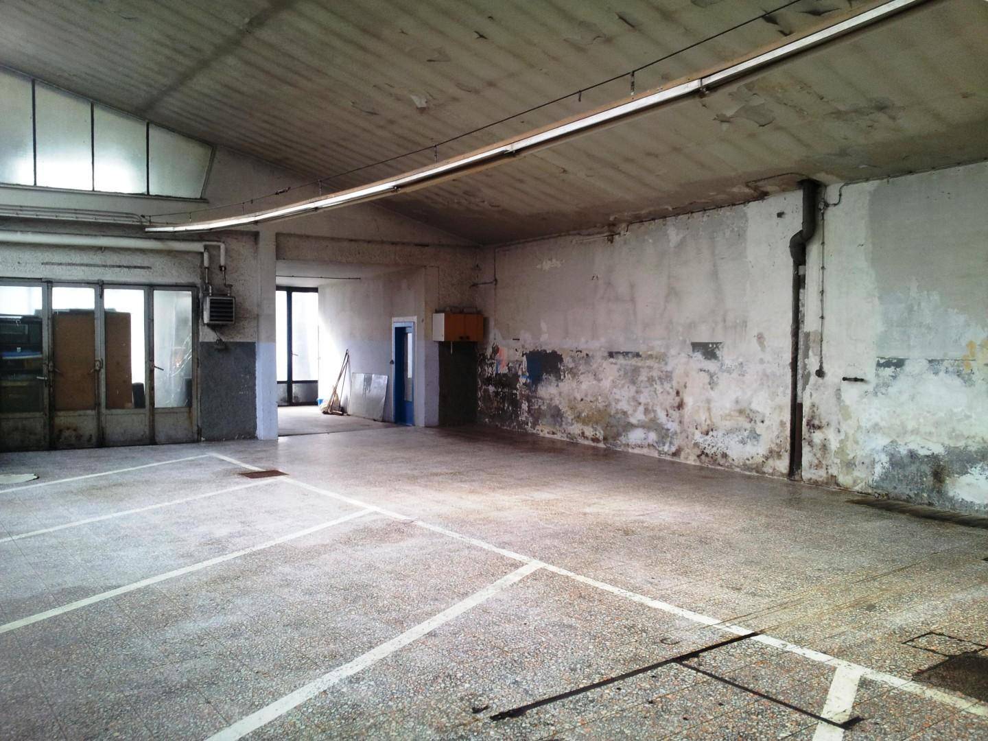 Große, leere Halle mit Betonboden, Parkplatzmarkierungen und sichtbaren Gebrauchsspuren an den Wänden.