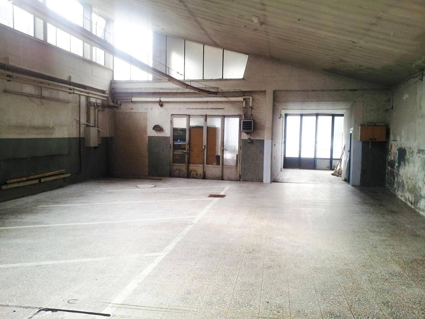 Weitläufige Halle mit Betonboden, Parkplatzmarkierungen und mehreren Zugängen.
