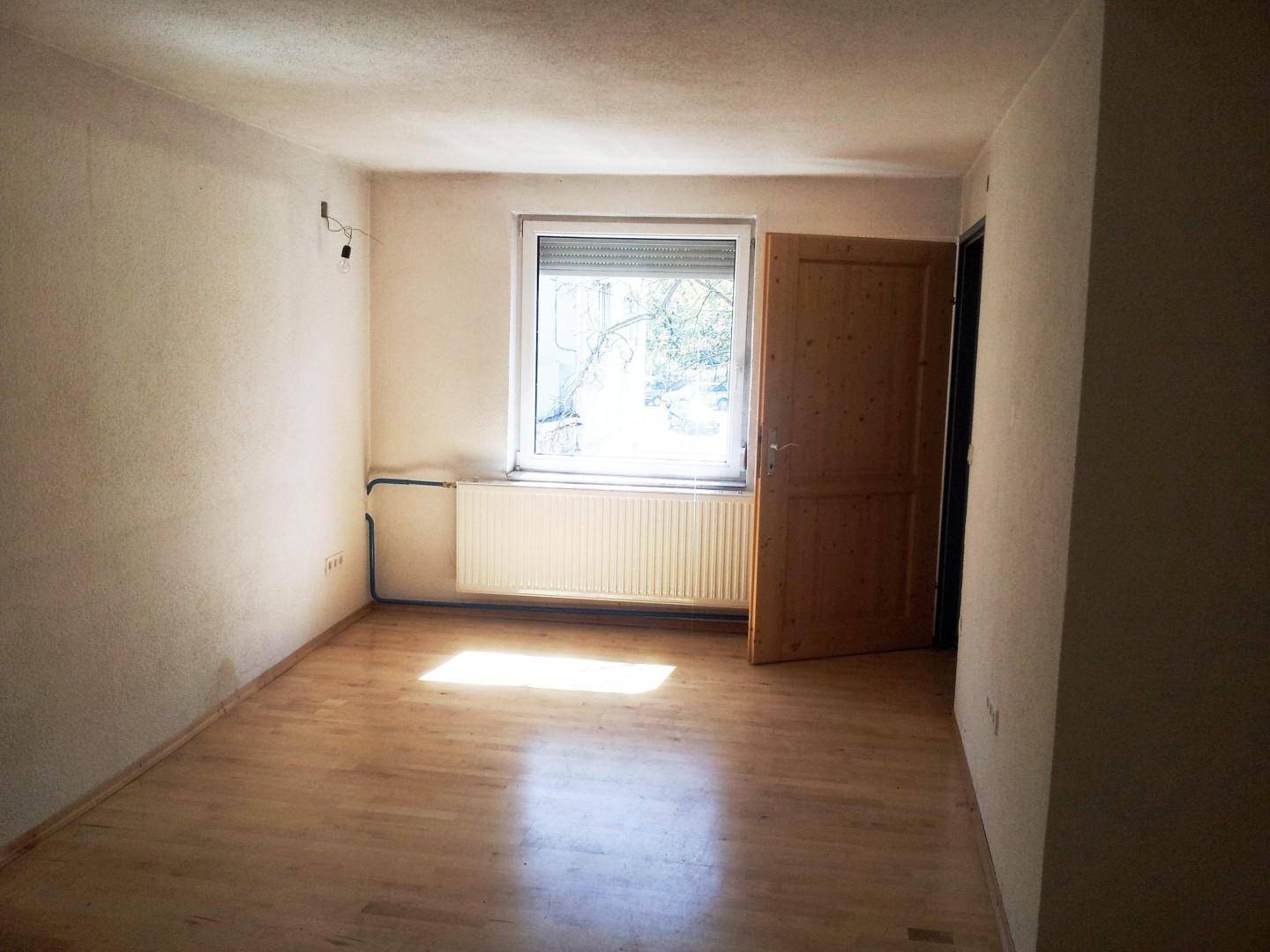 Helles Zimmer mit Holzboden und Fenster, bereit zur individuellen Gestaltung.