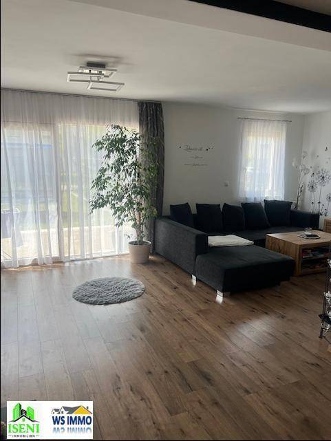 Helles Wohnzimmer mit Zugang zur Terrasse, großem Sofa und Laminatboden.