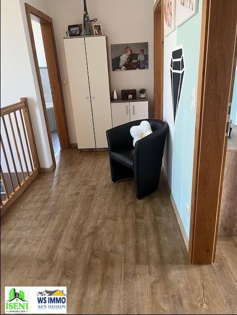 Heller Flurbereich im Obergeschoss mit Laminatboden, einem Sessel und dekorativer Wandgestaltung.