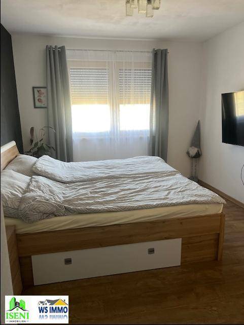 Gemütliches Schlafzimmer mit großem Doppelbett, Laminatboden und Blick auf die Fenster mit Rollos.