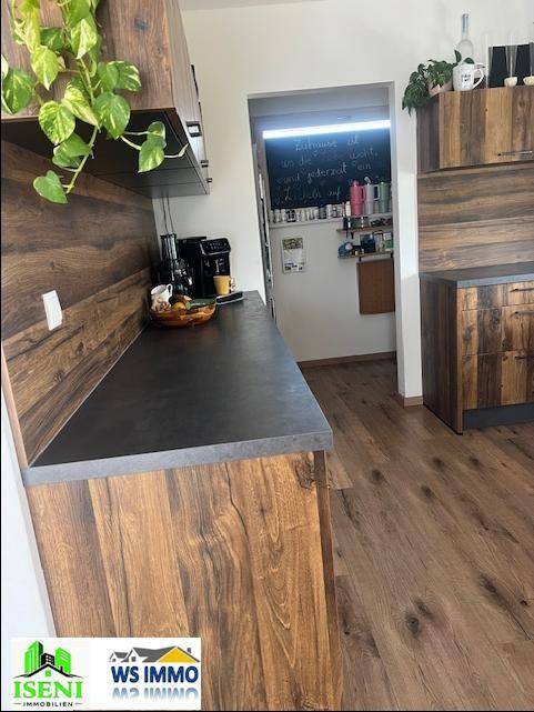 Küchenzeile mit Holzoptik-Schränken, dunkler Arbeitsplatte und Blick in einen angrenzenden Raum.