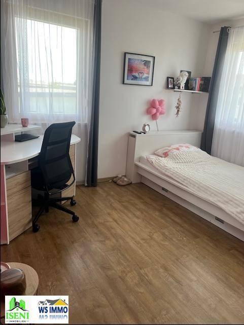 Jugendzimmer mit Bett, Schreibtisch und Bürostuhl, ausgestattet mit Laminatboden und großen Fenstern.