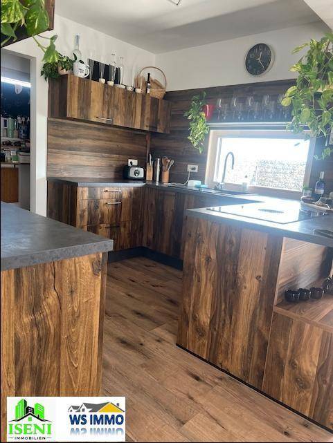 Moderne Küche mit Holzfronten, dunkler Arbeitsplatte und integriertem Kochfeld.