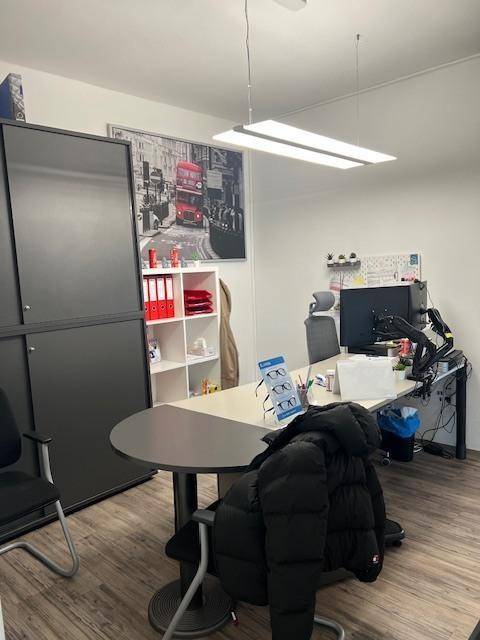 Büro mit Schreibtisch, Computer und einem runden Tisch, beleuchtet von einer modernen Deckenleuchte.