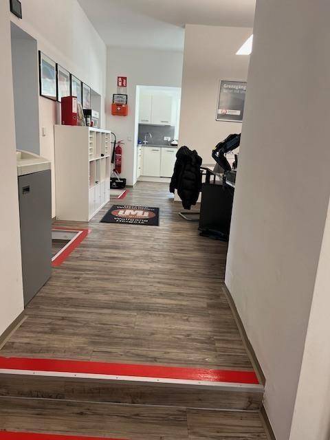 Empfangsbereich mit Laminatboden, Schreibtisch und Blick in eine kleine Küche im Hintergrund.