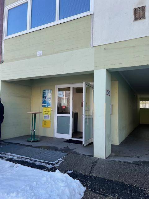 Eingangsbereich eines Gebäudes mit Glastür und Schnee auf dem Boden vor dem Gebäude.
