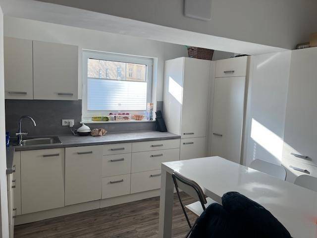 Moderne weiße Küche mit Einbauschränken, Spüle und einem Esstisch am Fenster.