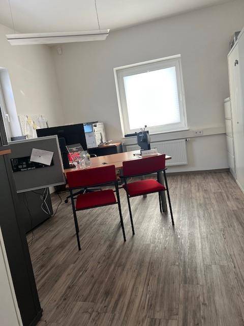 Geräumiges Büro mit Laminatboden, zwei roten Stühlen und einem Schreibtisch am Fenster.