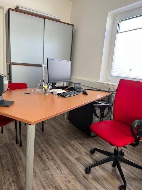 Helles Büro mit Holzboden, rotem Bürostuhl und einem Schreibtisch mit Computer.
