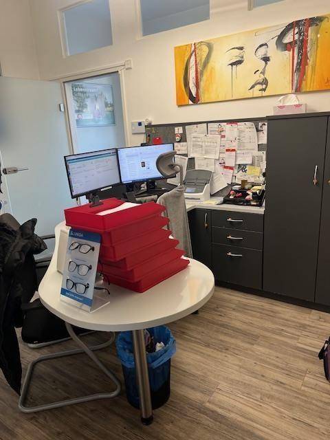 Büro mit zwei Monitoren, Schreibtisch und einem runden Tisch mit roten Präsentationsboxen.