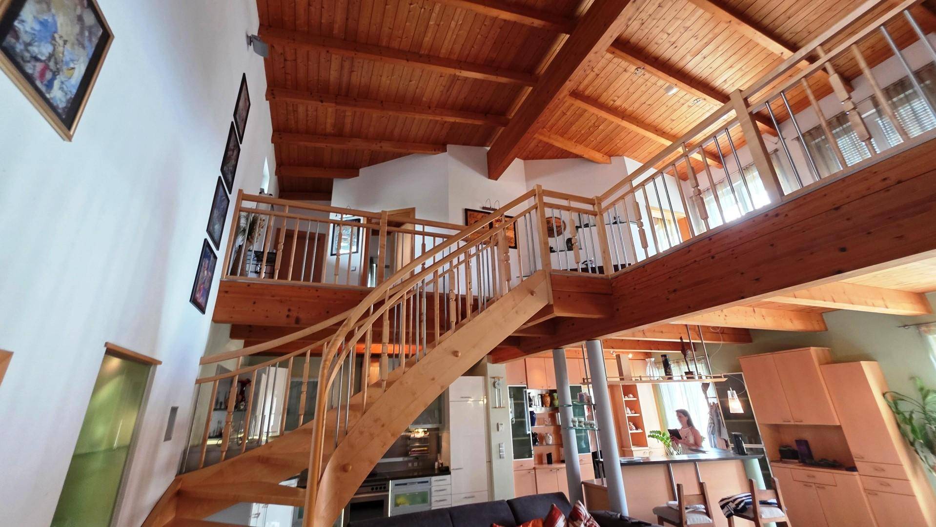 Heller, offener Wohnbereich mit einer eleganten Holztreppe, Galerie und sichtbaren Holzbalken an der Decke.