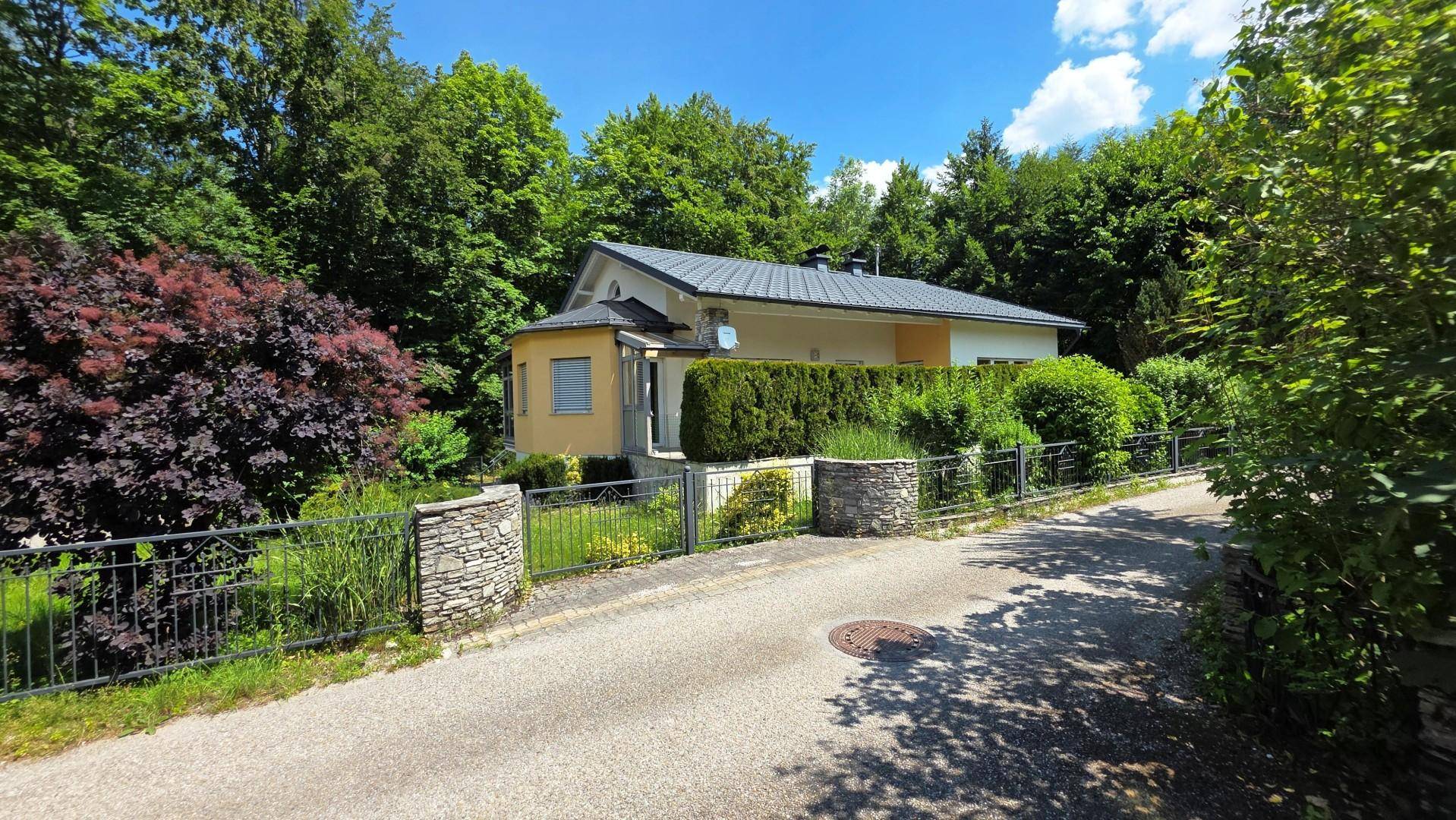 Das Haus ist von einem gepflegten Garten mit Hecken und Sträuchern umgeben, sichtbar von der Straße.