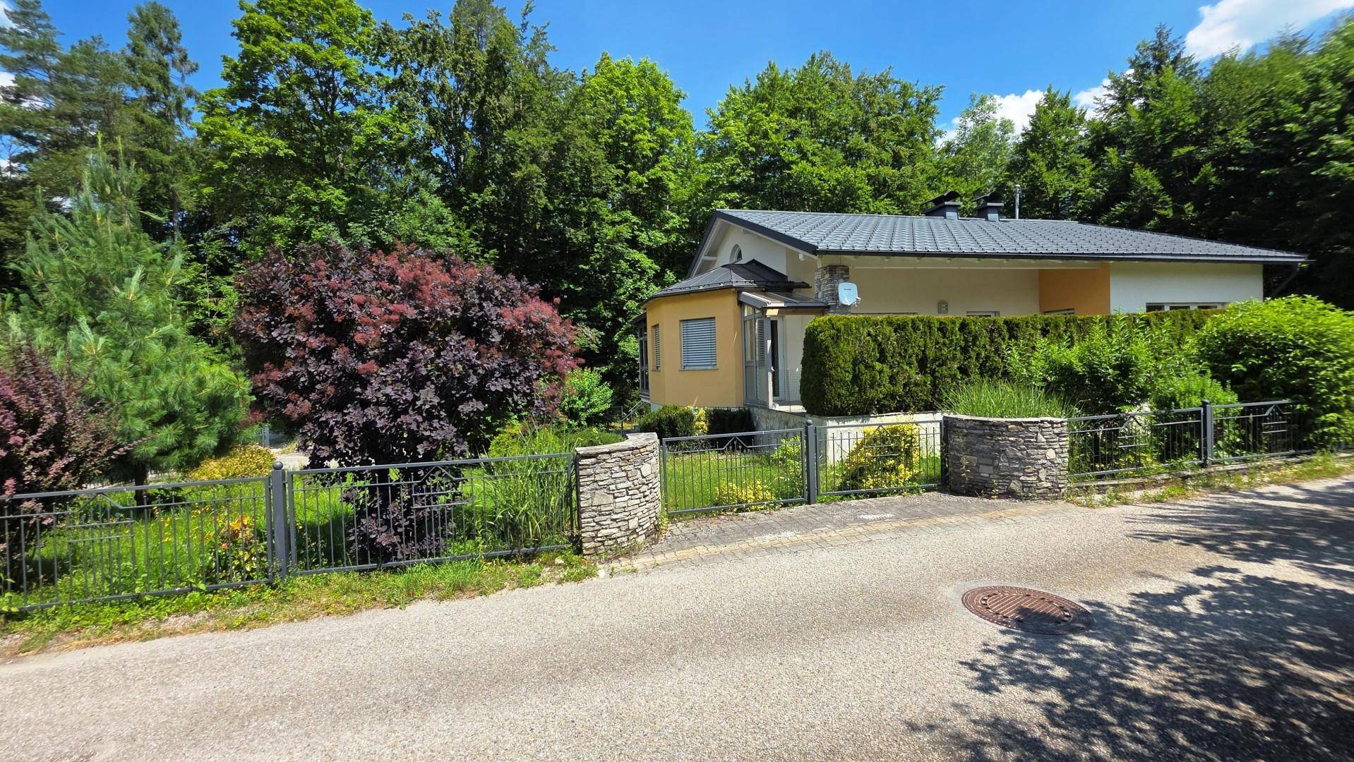 Ansicht des Hauses von der Straße, umgeben von einem grünen Garten mit Hecken und Bäumen.