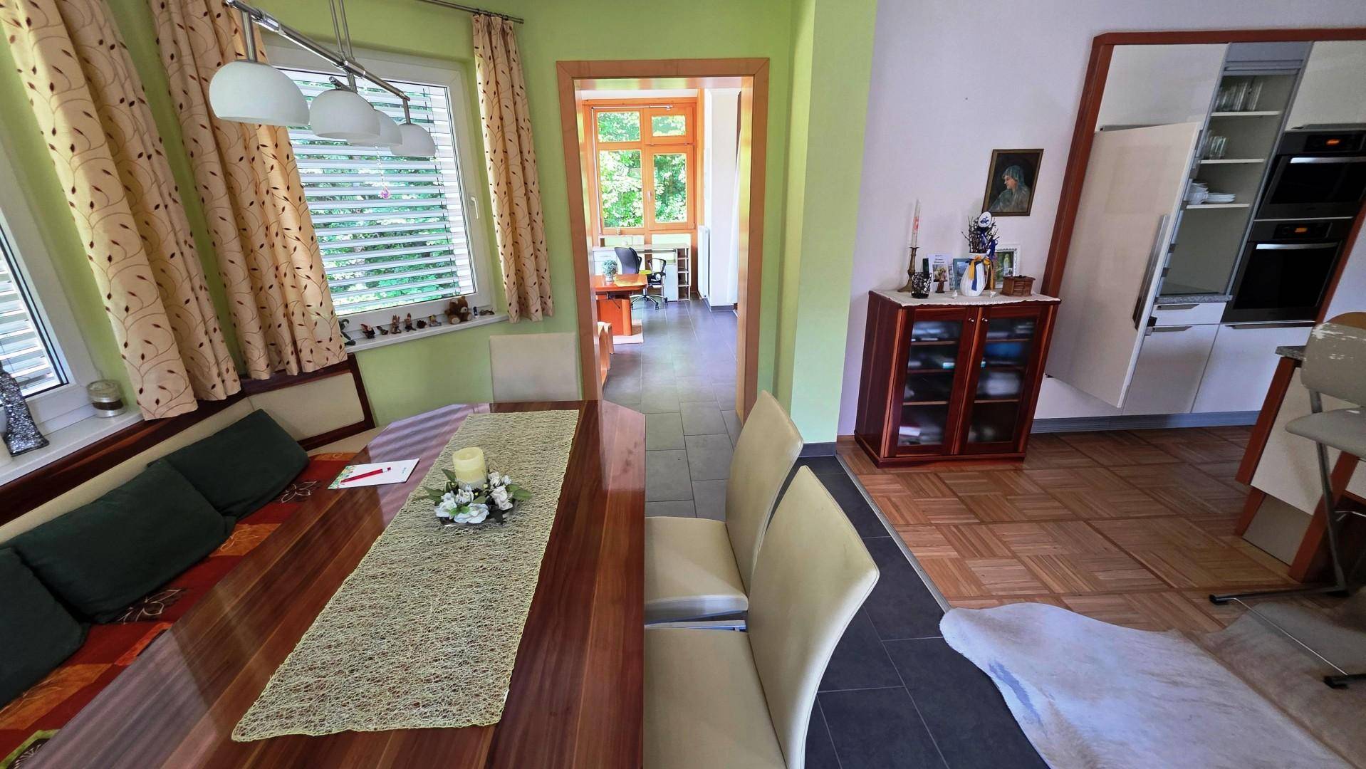 Essbereich mit Holztisch und Blick in die angrenzende Küche, helle Wände und Fliesenboden.
