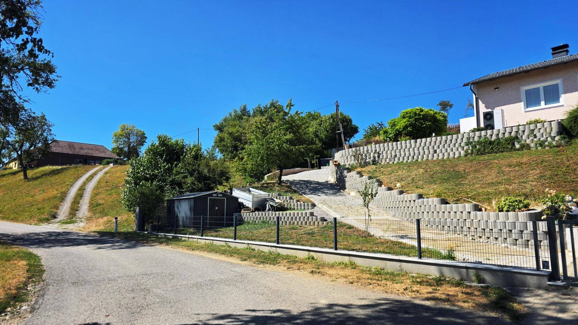 Weitläufige Ansicht des Anwesens von der Straße, mit Haus, terrassiertem Garten und ländlicher Umgebung.
