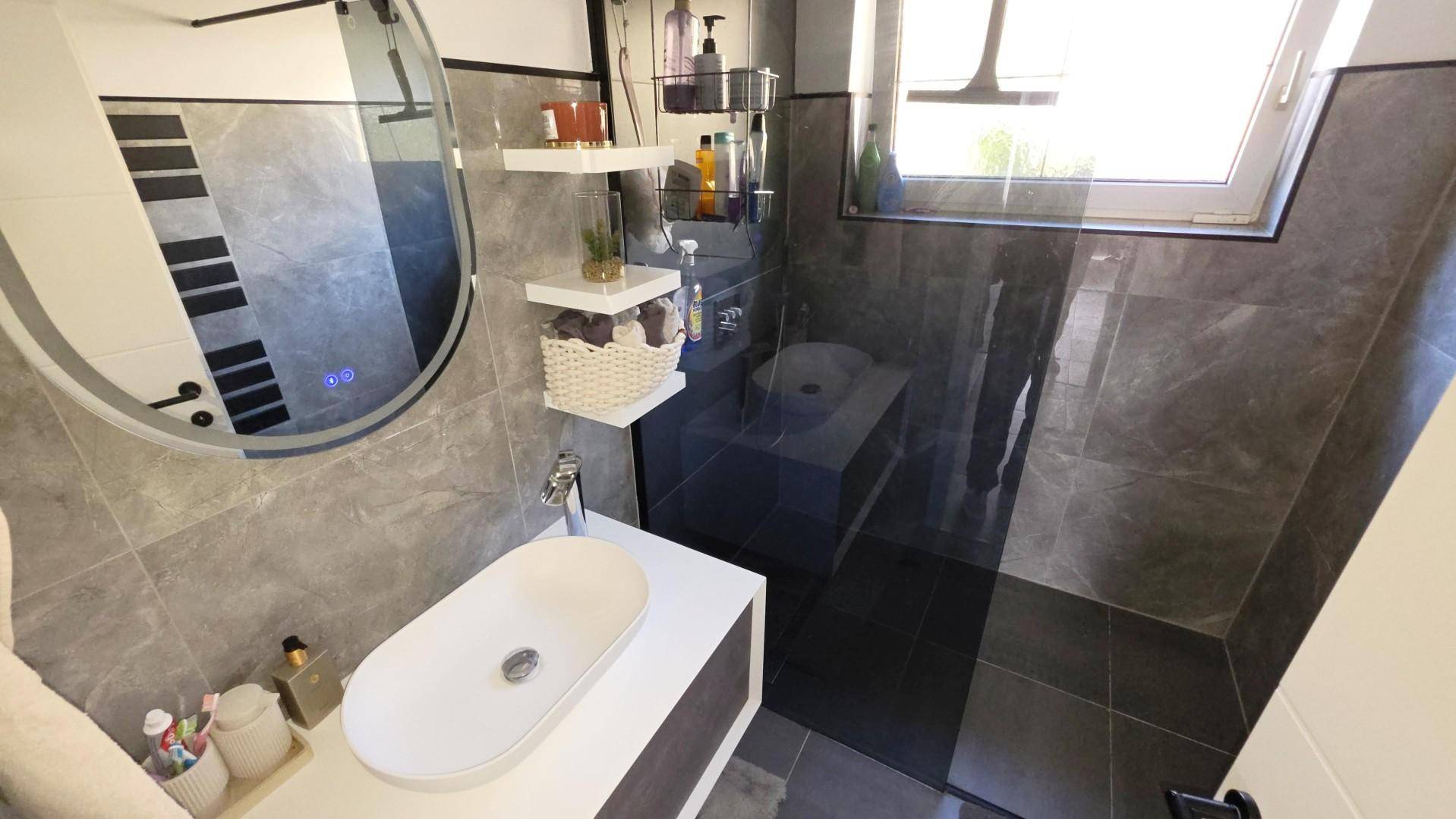 Modernes Badezimmer mit grauen Fliesen, ovalem Waschbecken und begehbarer Dusche.