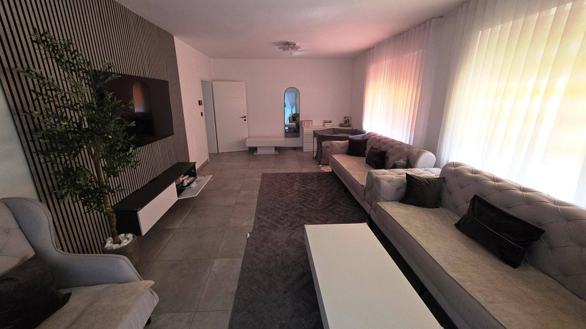 Modernes Wohnzimmer mit beigem Sofa, dunklem Teppich und dekorativer Wandverkleidung.