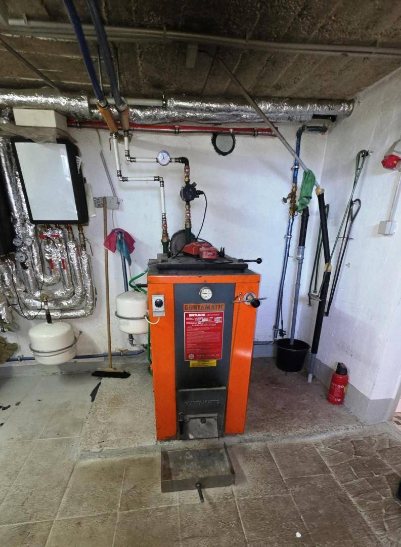 Heizungsraum mit großem orangefarbenen Heizkessel und komplexen Rohrleitungen an der Decke.