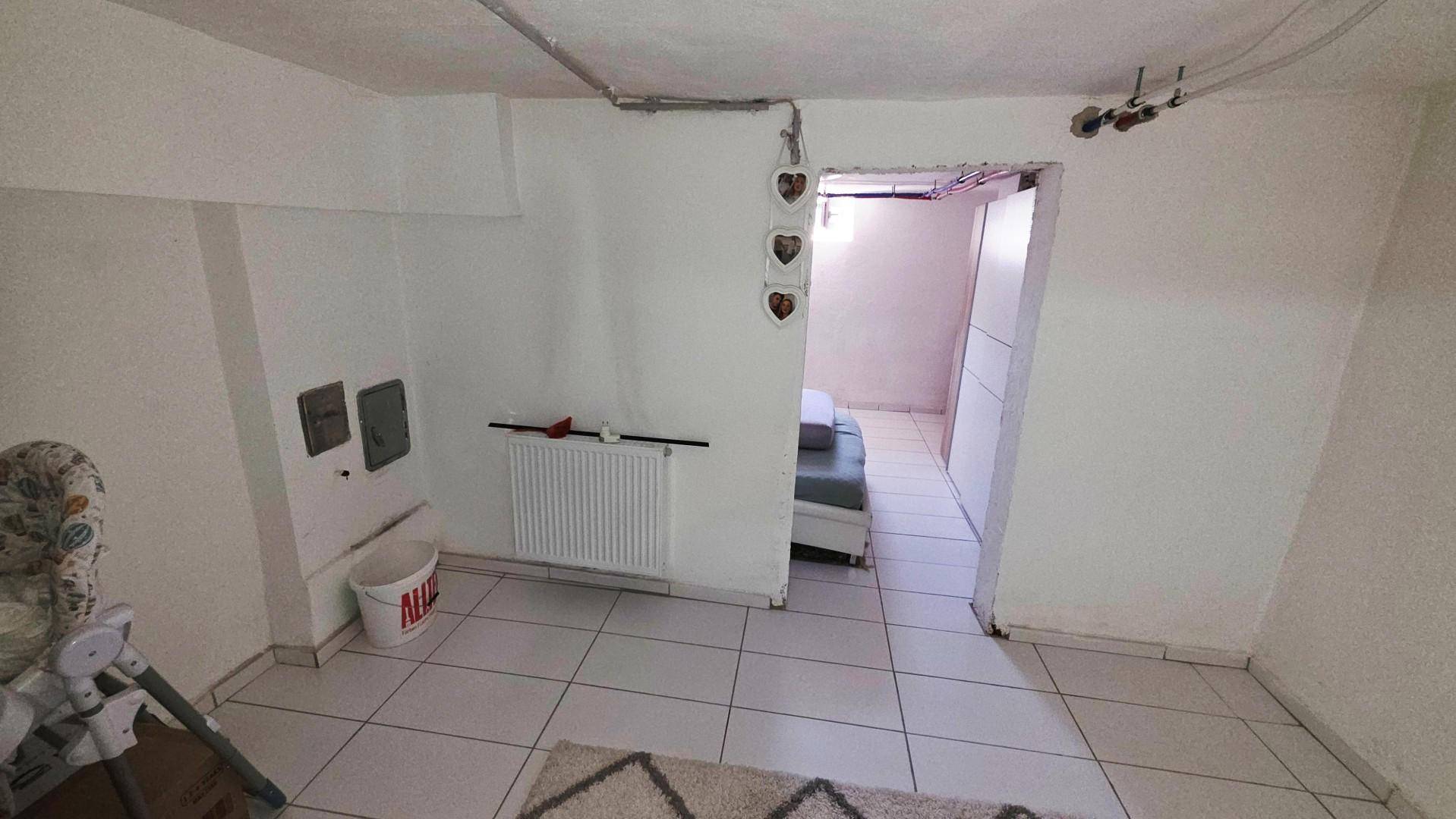Unfertiger Kellerraum mit Fliesenboden und Zugang zu einem weiteren Bereich.