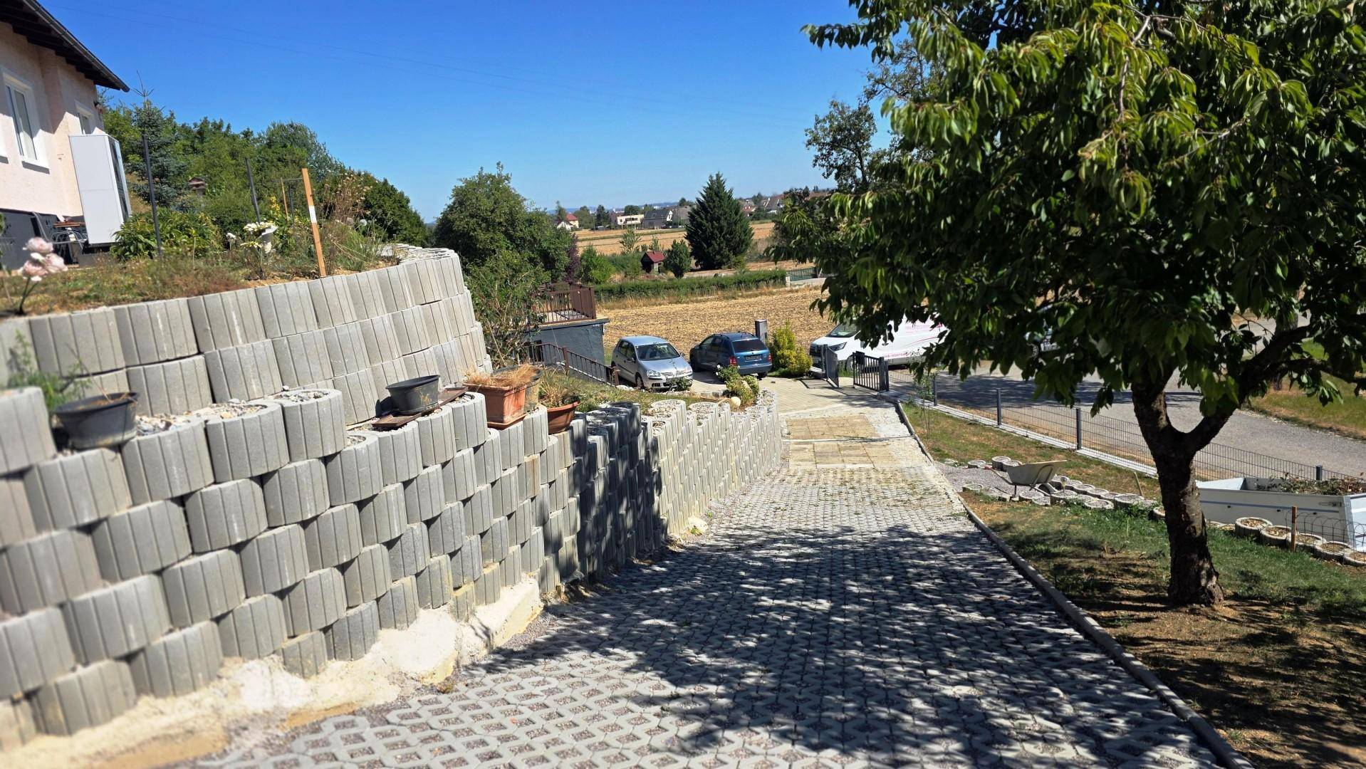 Gepflasterter Zufahrtsweg mit einer hohen Stützmauer und Blick auf die umliegende ländliche Gegend.