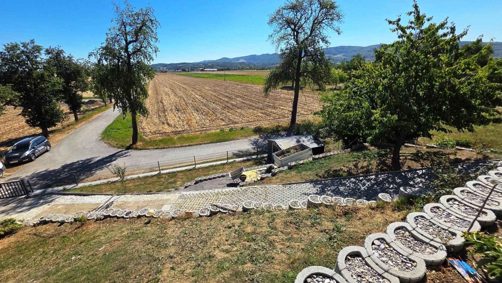 Blick auf den terrassierten Garten mit dekorativen Steinelementen und weitem Feldblick.