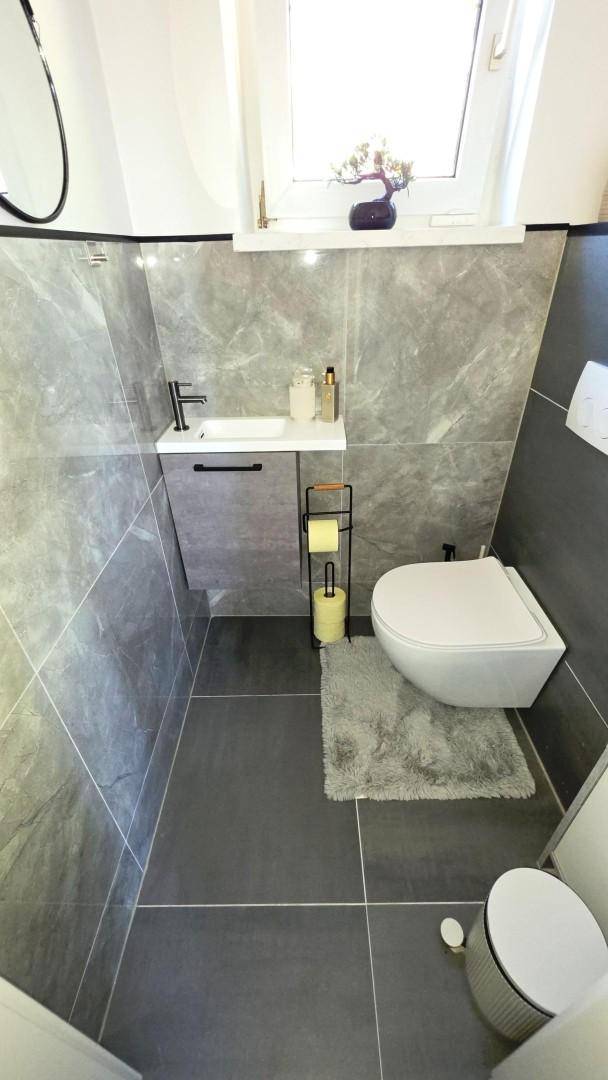 Modernes Gäste-WC mit wandhängender Toilette, kleinem Waschbecken und Fenster.