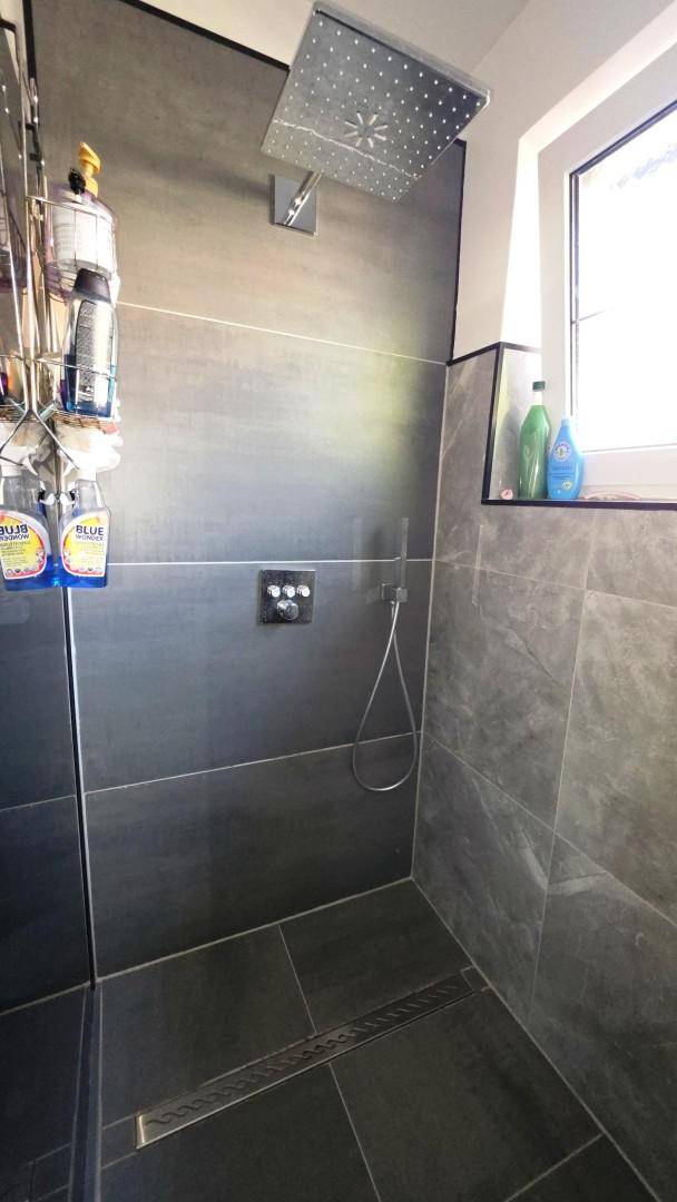 Geräumige begehbare Dusche mit Regenduschkopf und großformatigen Fliesen.