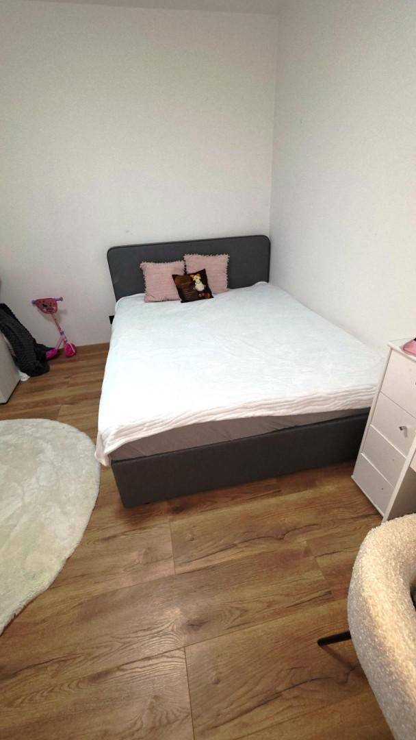 Helles Schlafzimmer mit Doppelbett, Holzfußboden und minimalistischer Einrichtung.