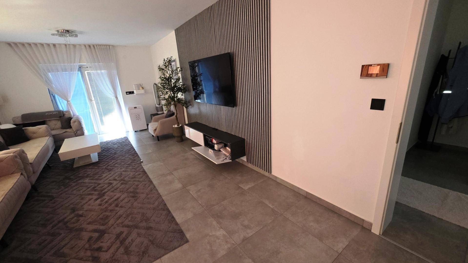 Geräumiges Wohnzimmer mit moderner Wandgestaltung, Fliesenboden und viel Tageslicht.