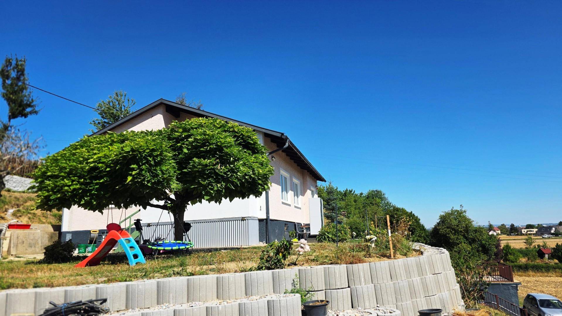 Einfamilienhaus mit Spielbereich im Garten und Panoramablick auf die umliegende grüne Landschaft.