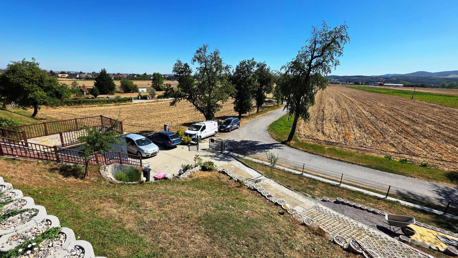 Weitläufiger Blick auf die ländliche Umgebung mit Feldern, Bäumen, Straße und Parkplatz.
