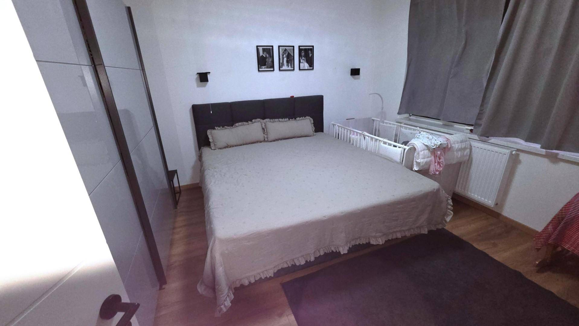 Schlafzimmer mit Doppelbett, Babybett und Holzfußboden, ausgestattet mit Kleiderschrank.
