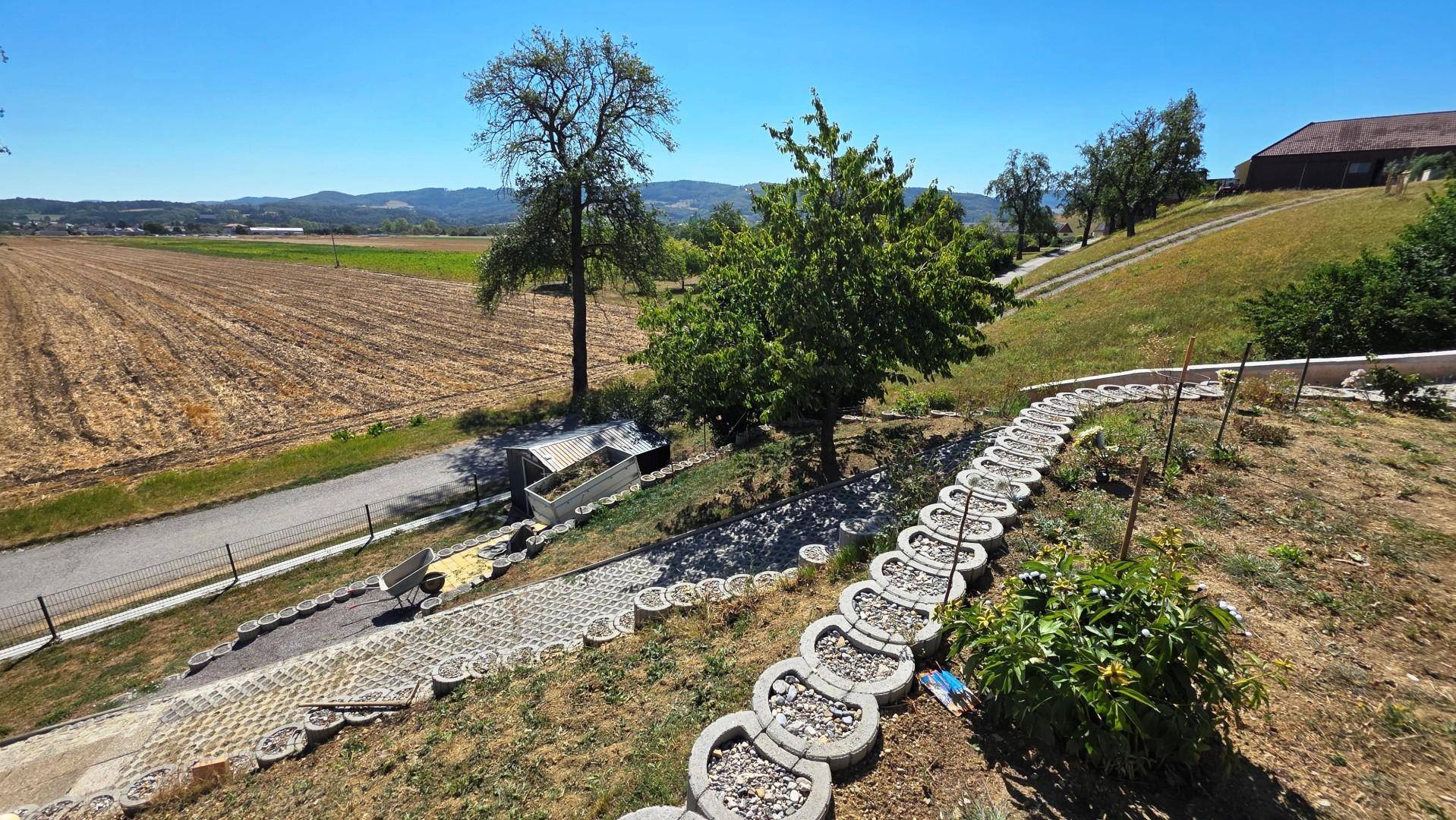 Blick auf den terrassierten Garten mit dekorativen Steinelementen und weitem Feldblick.