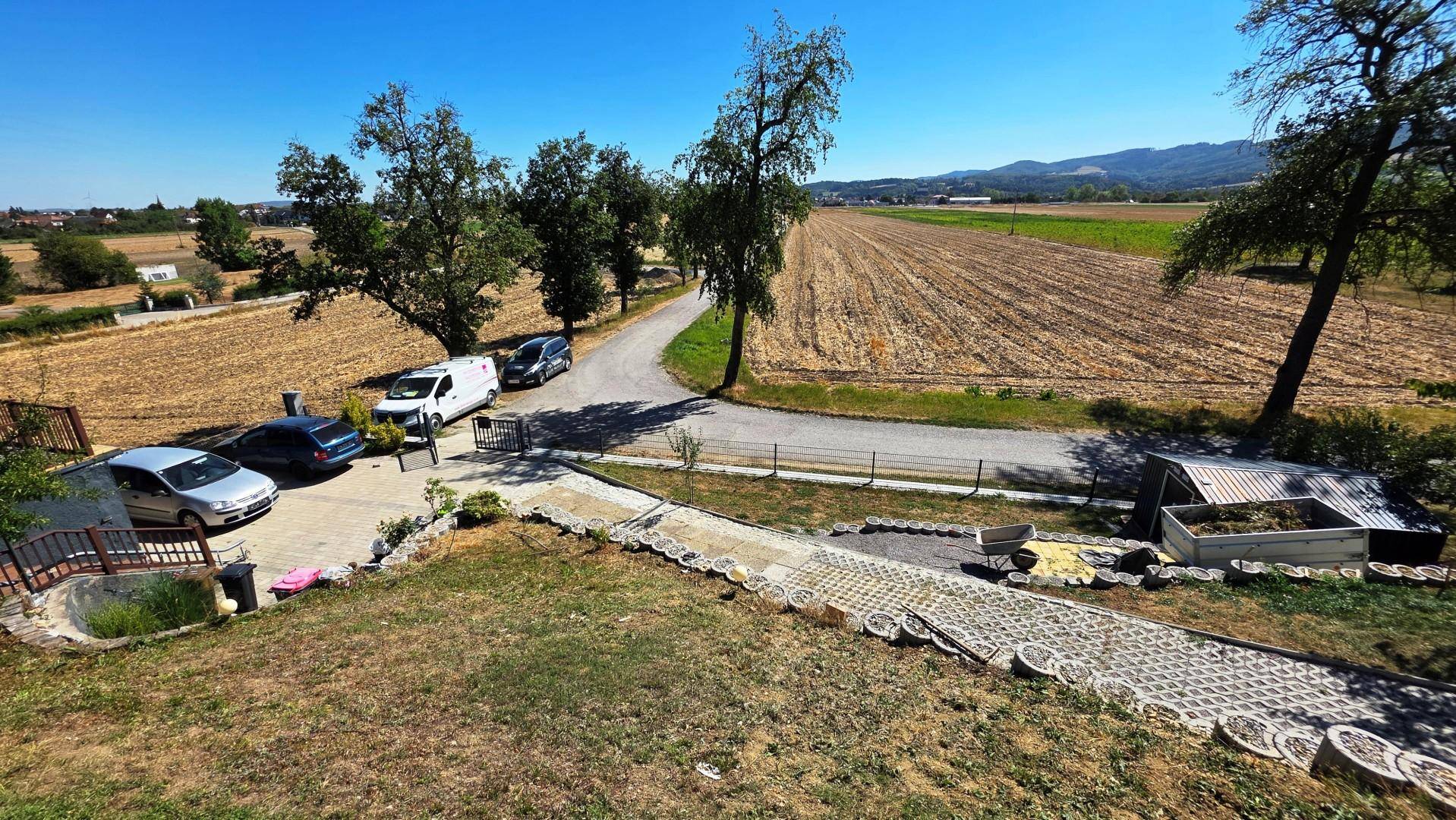 Weitläufiger Blick auf die ländliche Umgebung mit Feldern, Bäumen, Straße und Parkplatz.
