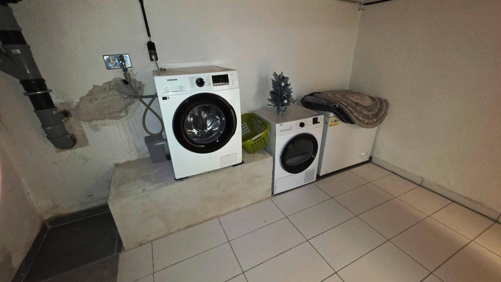 Waschküche im Keller mit Waschmaschine, Trockner und Gefrierschrank auf Fliesenboden.