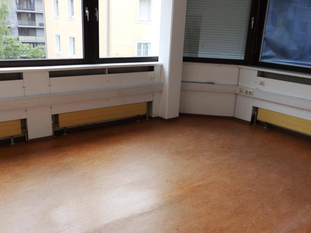 Eckbereich eines Büroraums mit Fenstern, die einen Blick auf Gebäude und Grünflächen ermöglichen.