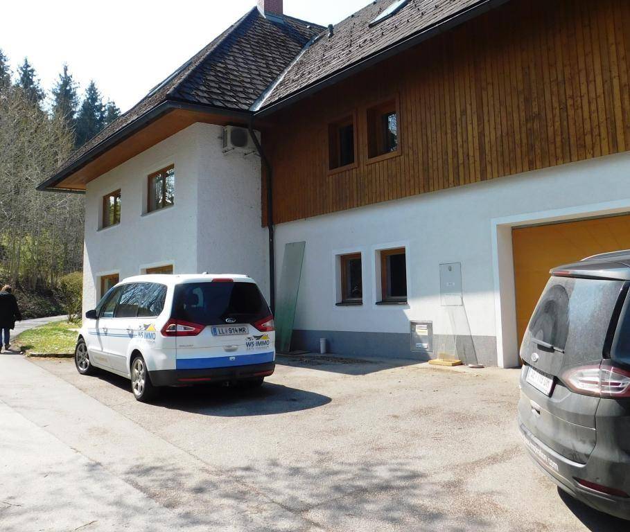 Außenansicht des Hauses mit weißer Fassade, Holzverkleidung und Stellplätzen für Fahrzeuge.