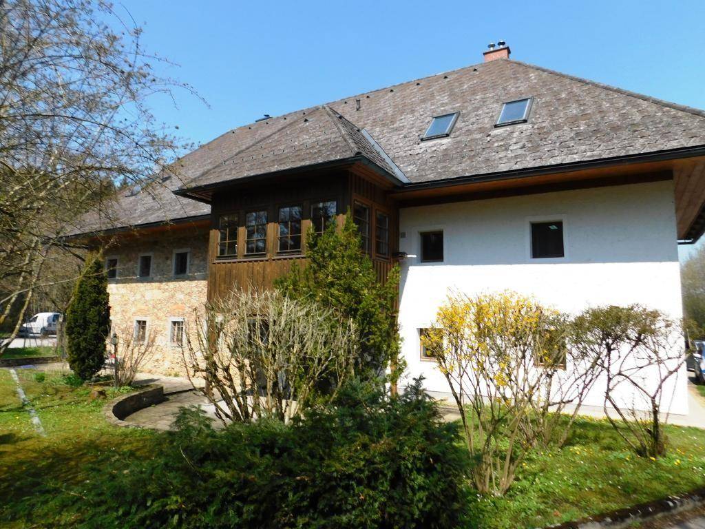 Idyllische Außenansicht des Hauses mit Garten, alten Bäumen und traditioneller Architektur.