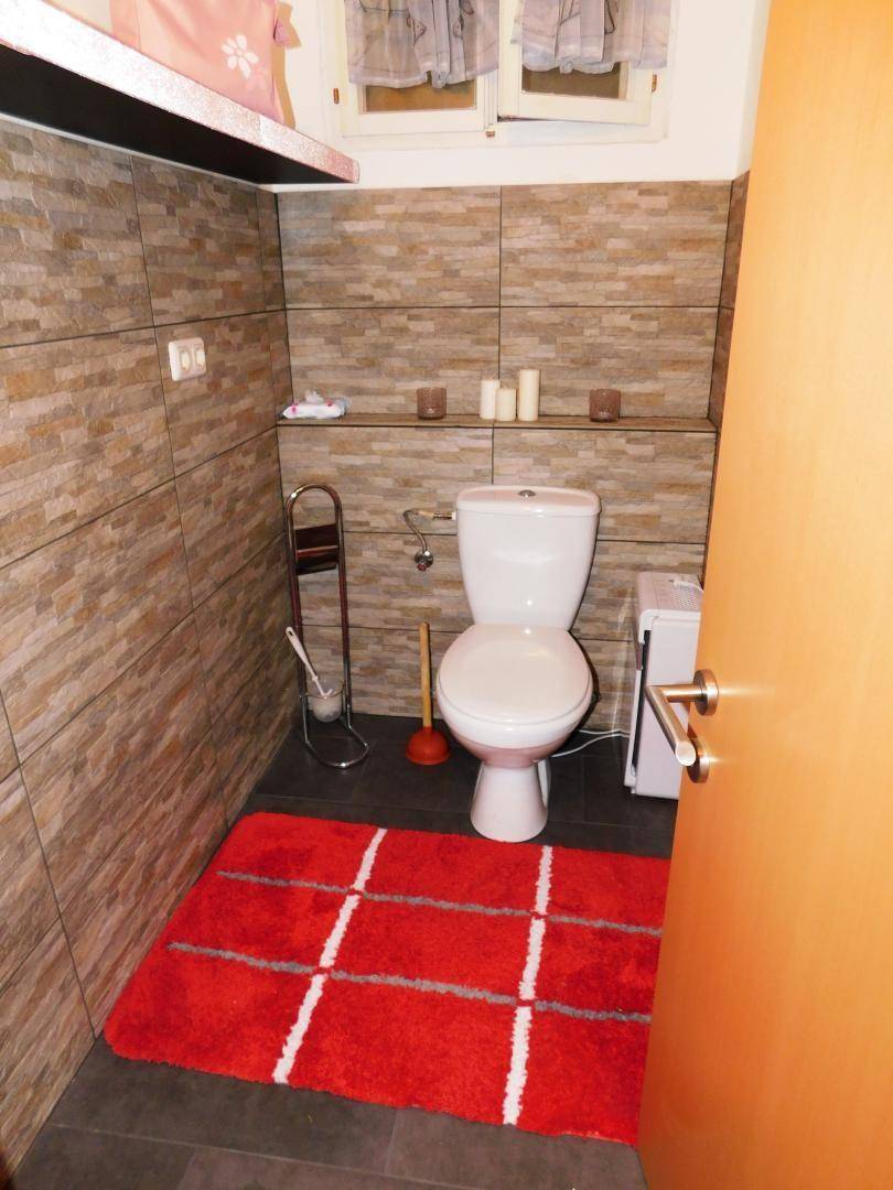 Separate Toilette mit Wandfliesen in Steinoptik und einem roten Teppich, funktional eingerichtet.