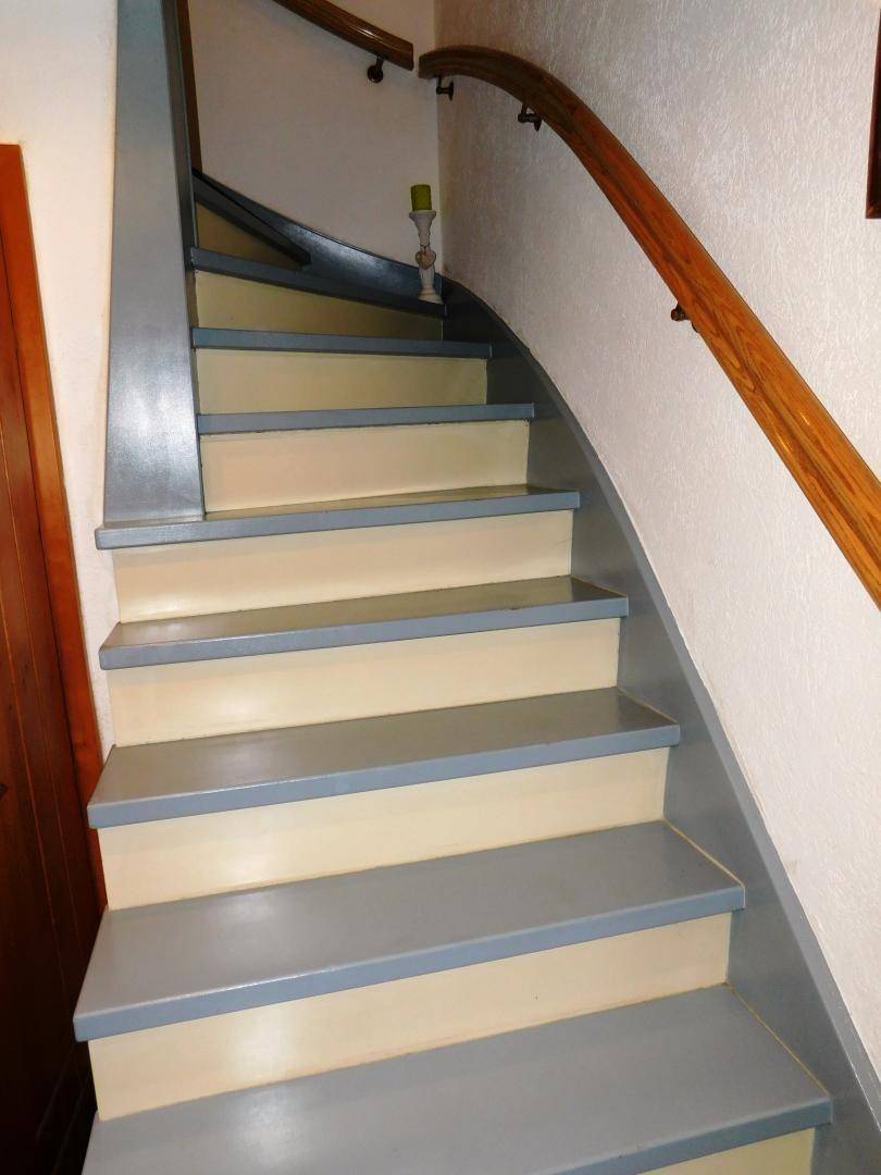 Geschwungene Treppe mit Holzgeländer und hellgrau gestrichenen Stufen in einem Flur.