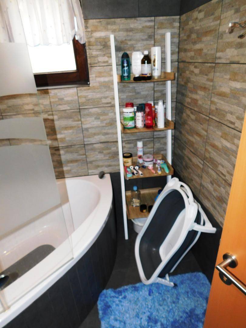 Badezimmer mit Badewanne, beigefarbenen Wandfliesen und einem kleinen Fenster für Tageslicht.
