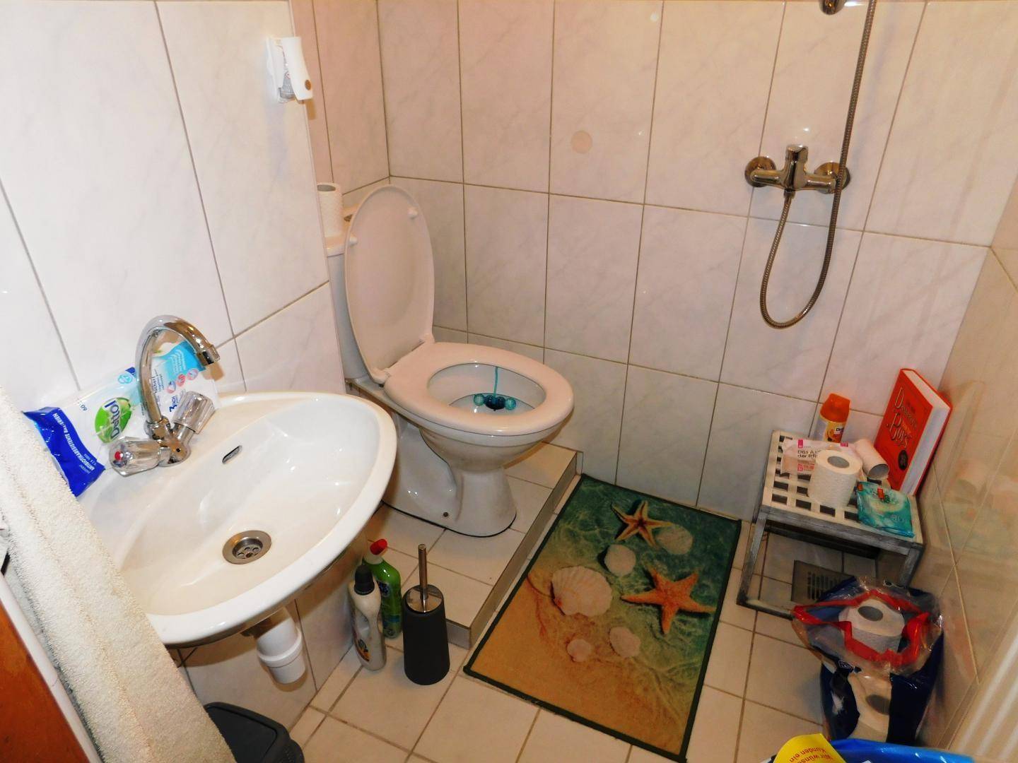 Kleines Badezimmer mit WC, Waschbecken und Duschvorrichtung, komplett mit weißen Fliesen ausgestattet.